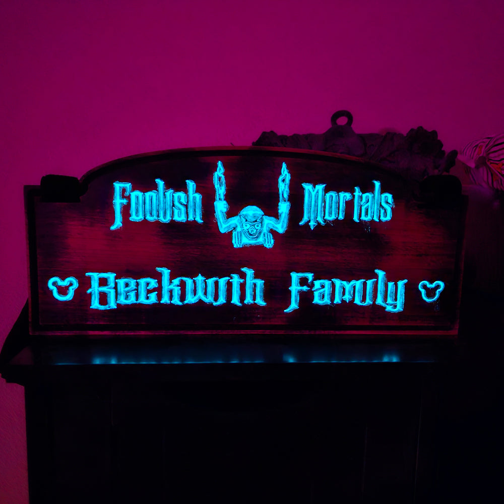 A stroller sign with the words Foolish Mortals and Beckwith Family in blue glow in the dark paint.