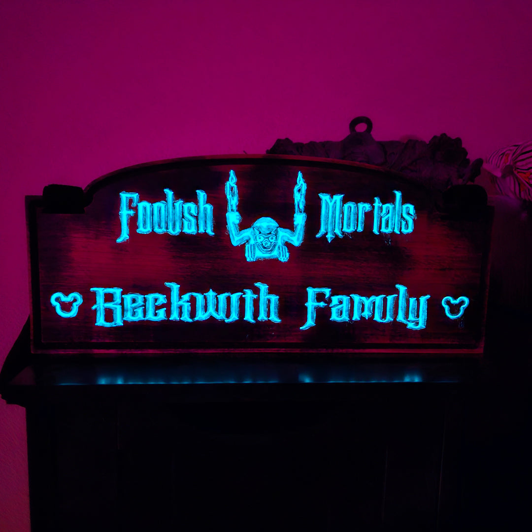 A stroller sign with the words Foolish Mortals and Beckwith Family in blue glow in the dark paint.
