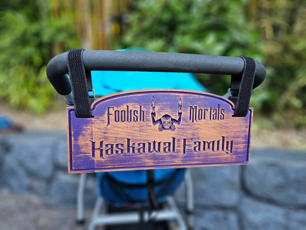 Wooden stroller sign with depicting a gargoyle with the words Foolish Mortals and Kaskawal Family finished in purple.