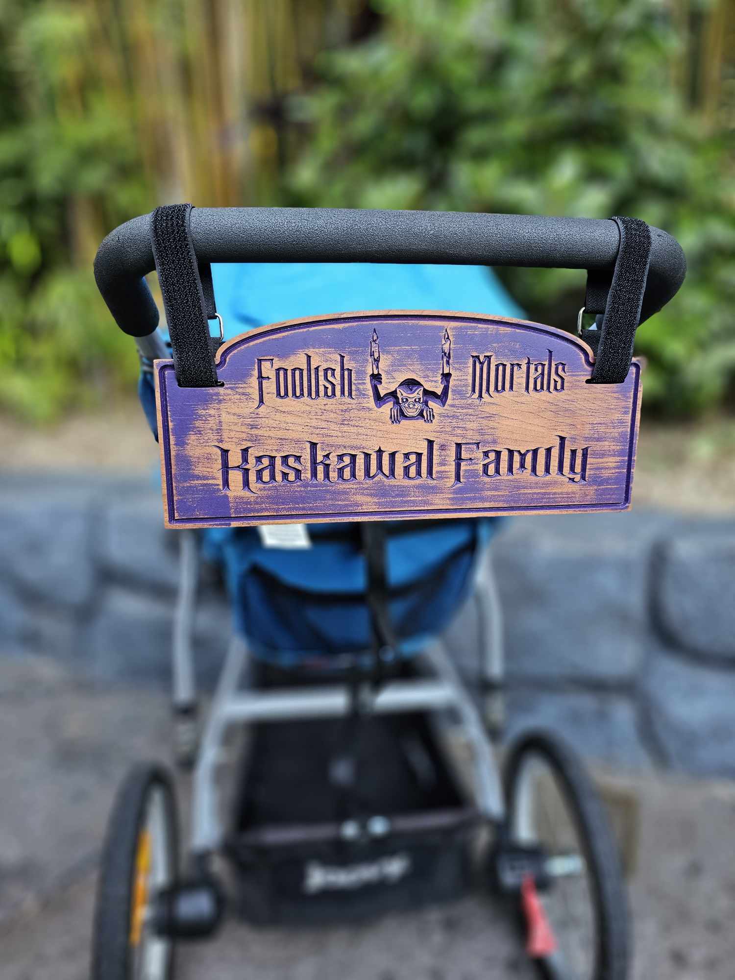 Wooden stroller sign with depicting a gargoyle with the words Foolish Mortals and Kaskawal Family finished in purple.