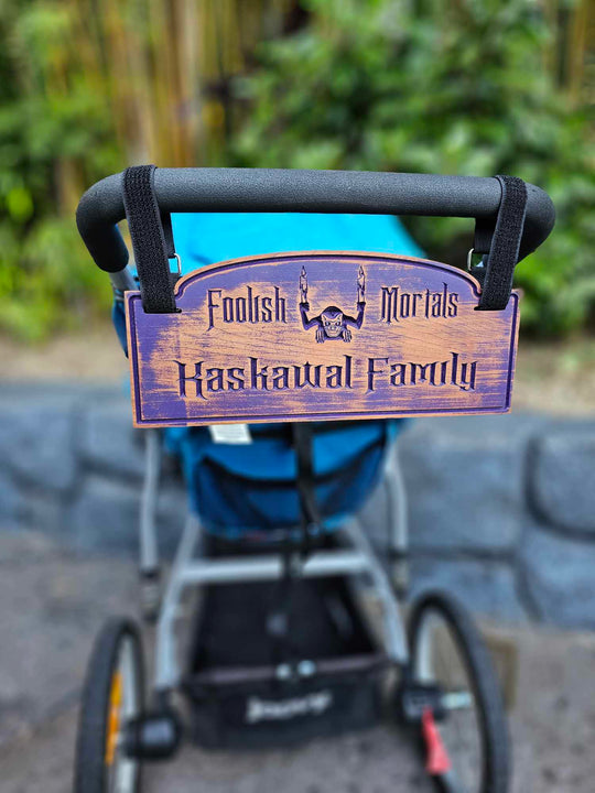 Wooden stroller sign with depicting a gargoyle with the words Foolish Mortals and Kaskawal Family finished in purple.