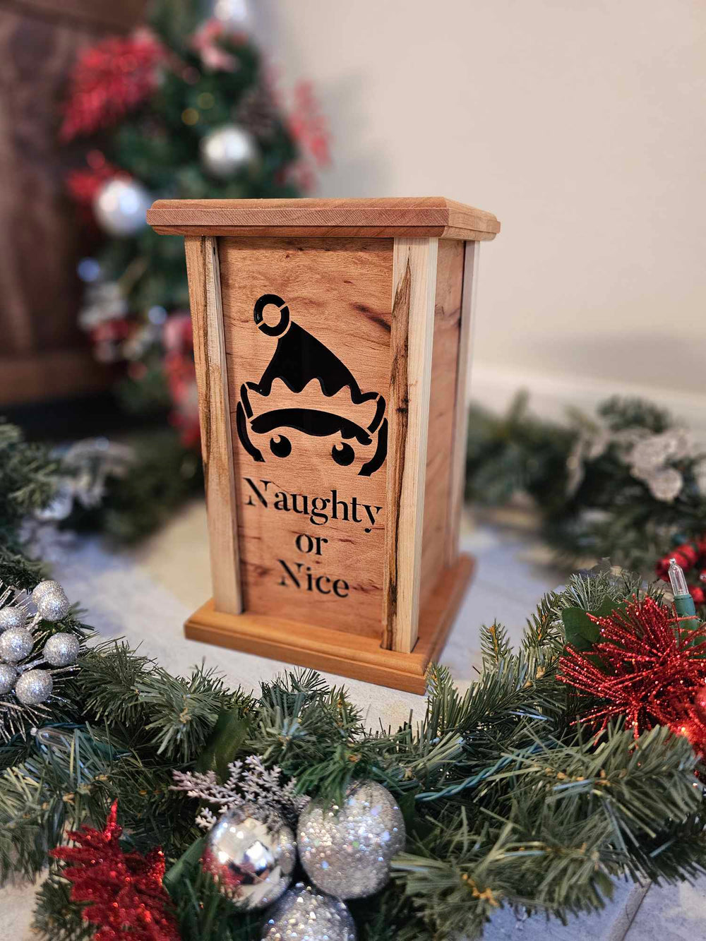 Wooden lantern face depicting a elf and the words naughty or nice.