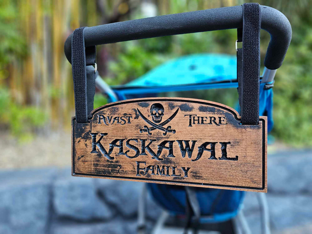 Wooden stroller sign hanging from stroller with hook and loop straps showing a skull and cross bones with the words Avast there and Kaskawal Family.