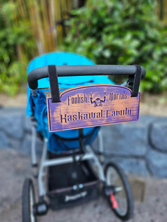 Wooden stroller sign with depicting a gargoyle with the words Foolish Mortals and Kaskawal Family finished in purple.
