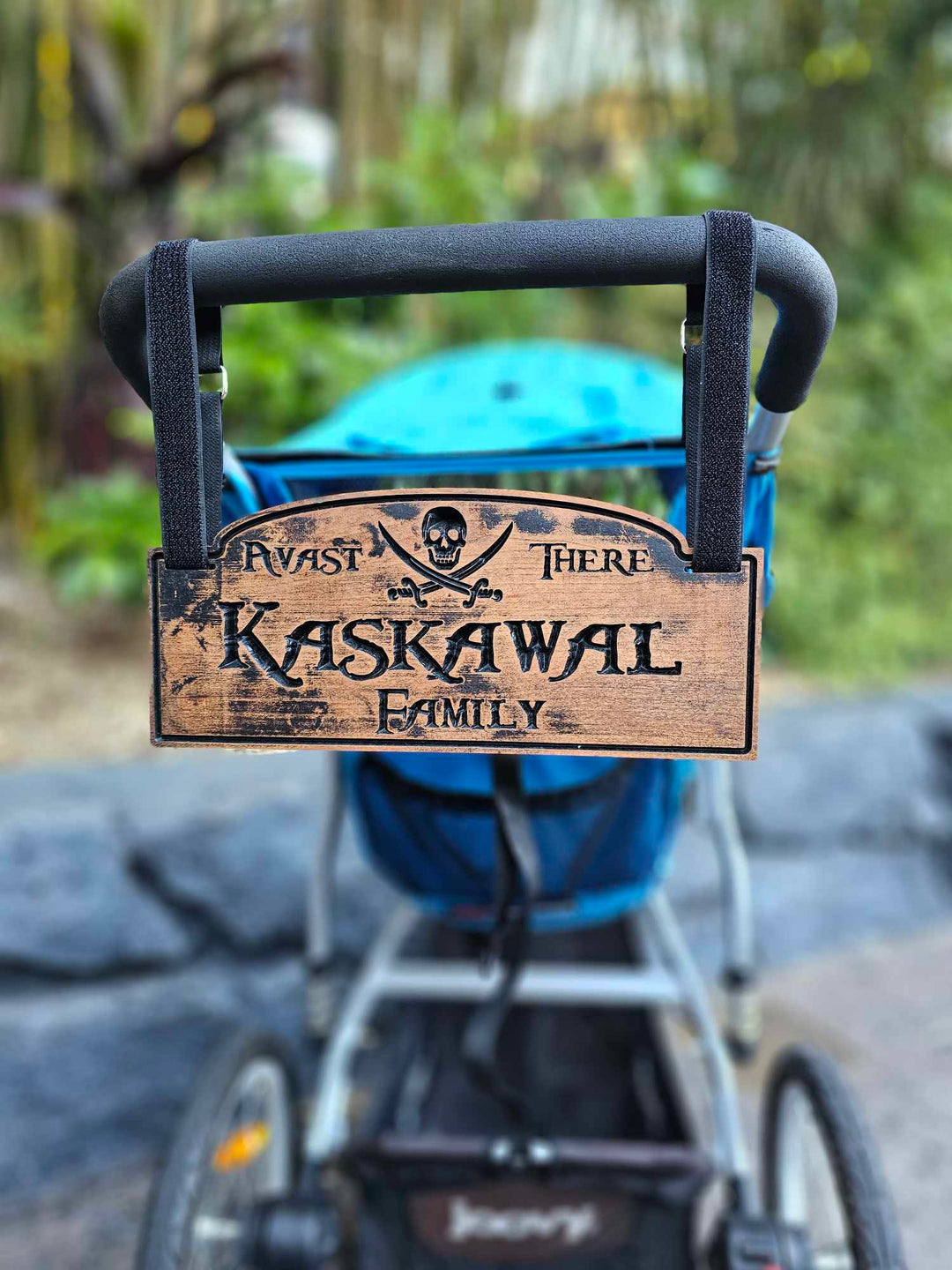 Wooden stroller sign hanging from stroller with hook and loop straps showing a skull and cross bones with the words Avast there and Kaskawal Family.