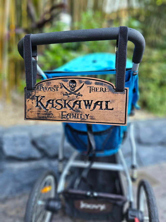 Wooden stroller sign hanging from stroller with hook and loop straps showing a skull and cross bones with the words Avast there and Kaskawal Family.