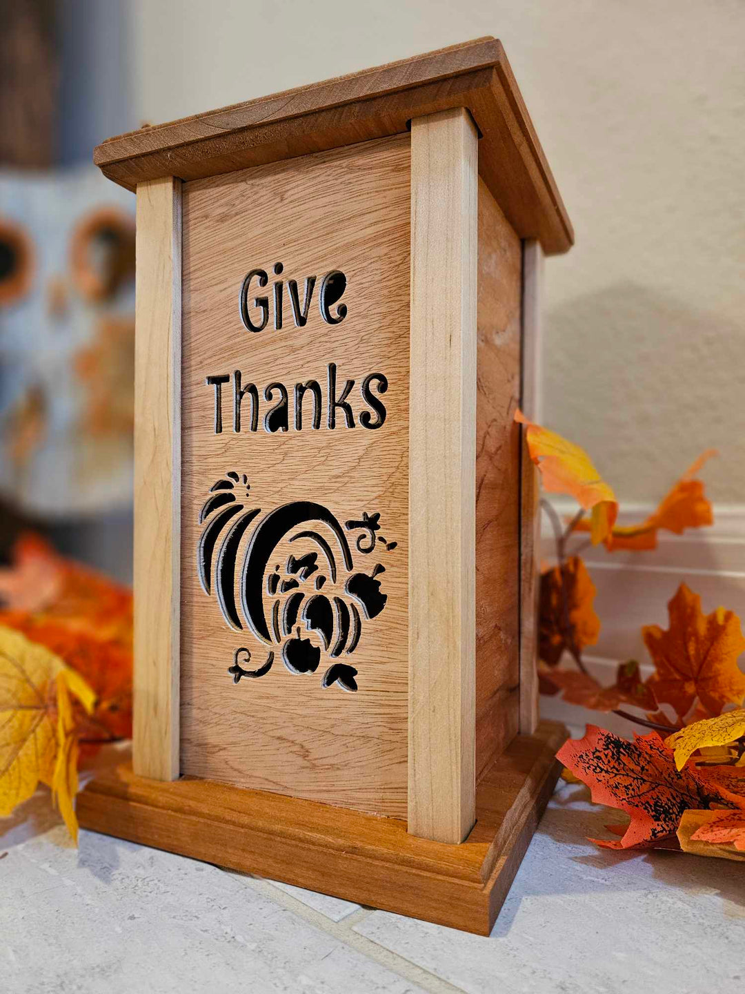 Wooden lantern face depicting a cornucopia and the phrase "Give Thanks".