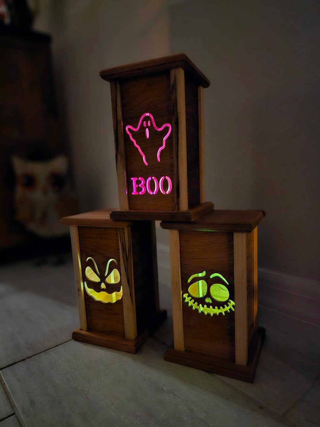 Three wooden lanterns with lantern faces depicting a ghost with the words boo, a sinister laughing face, and silly ghoul face.