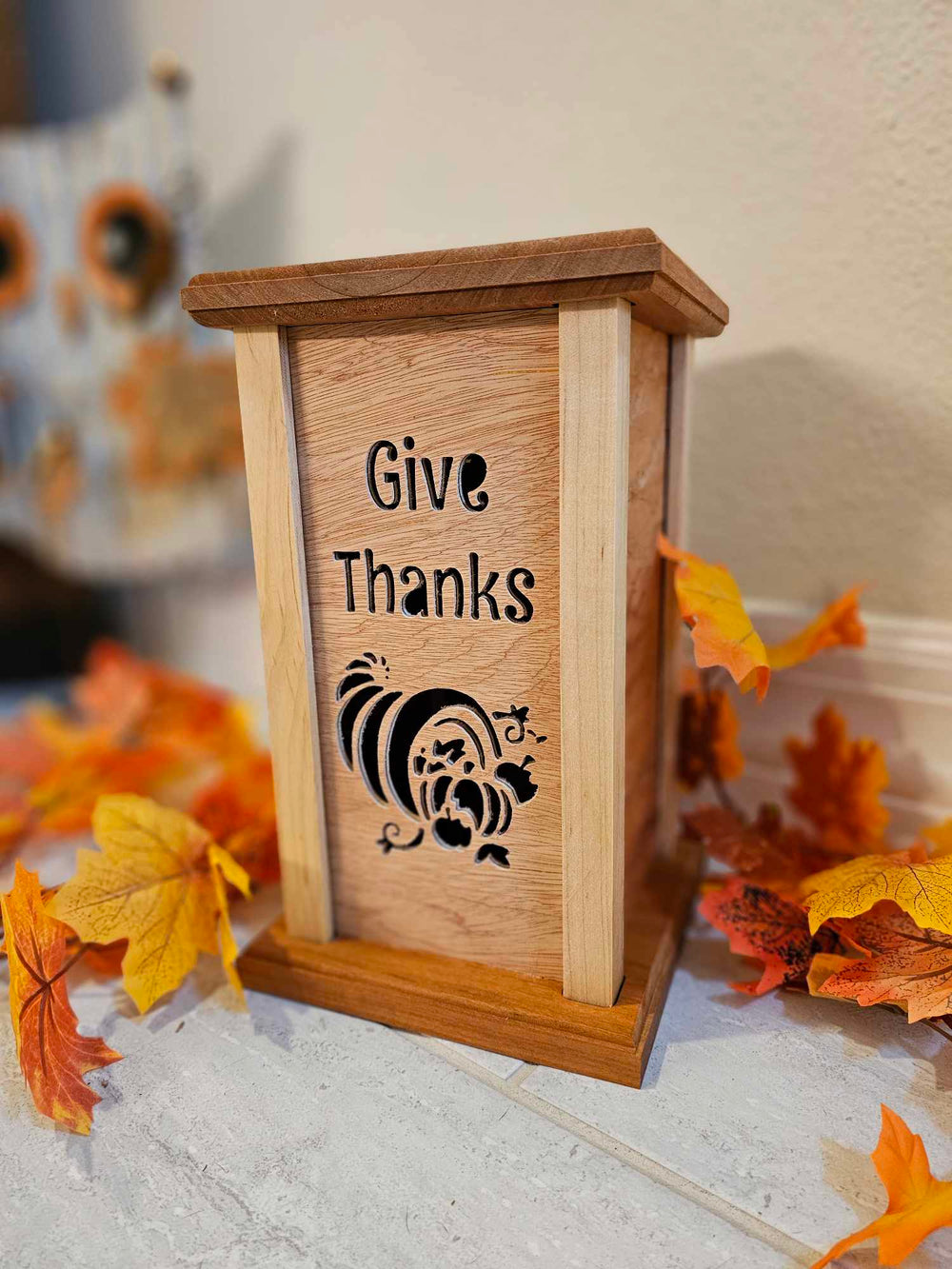 Wooden lantern face depicting a cornucopia and the phrase "Give Thanks".