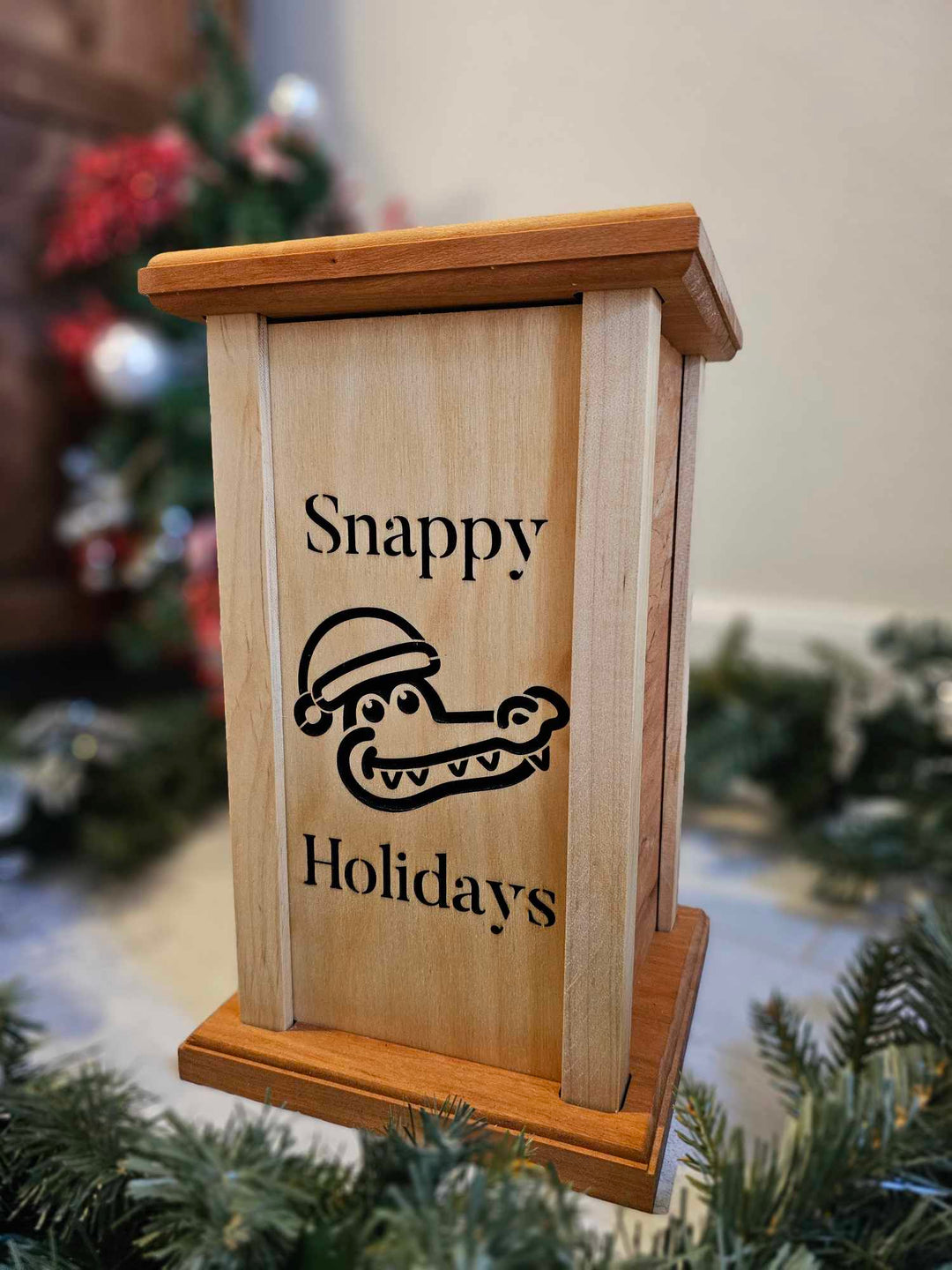 Wooden lantern face showing an alligator in a Santa hat with the words Snappy Holidays.