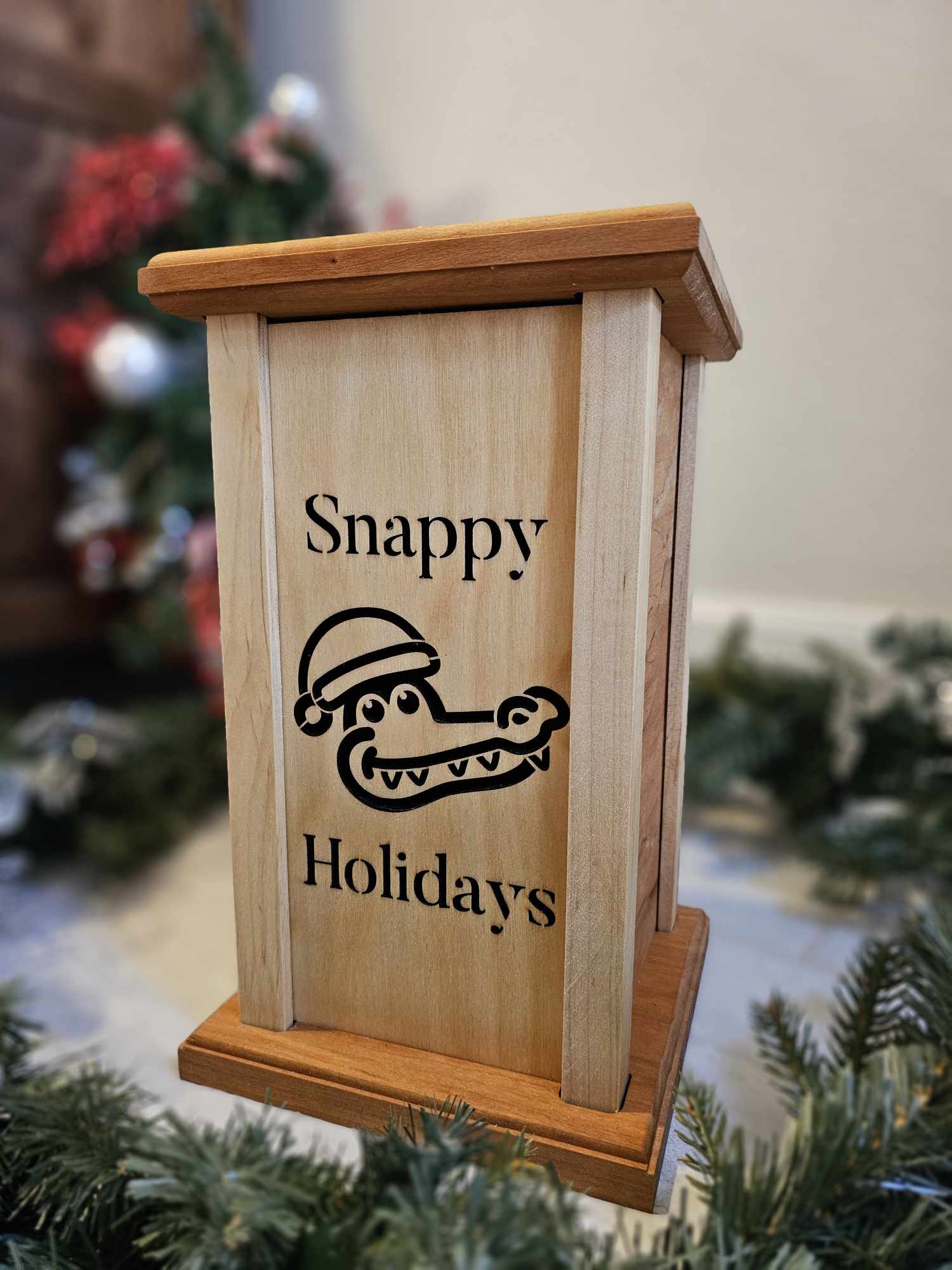 Wooden lantern face showing an alligator in a Santa hat with the words Snappy Holidays.