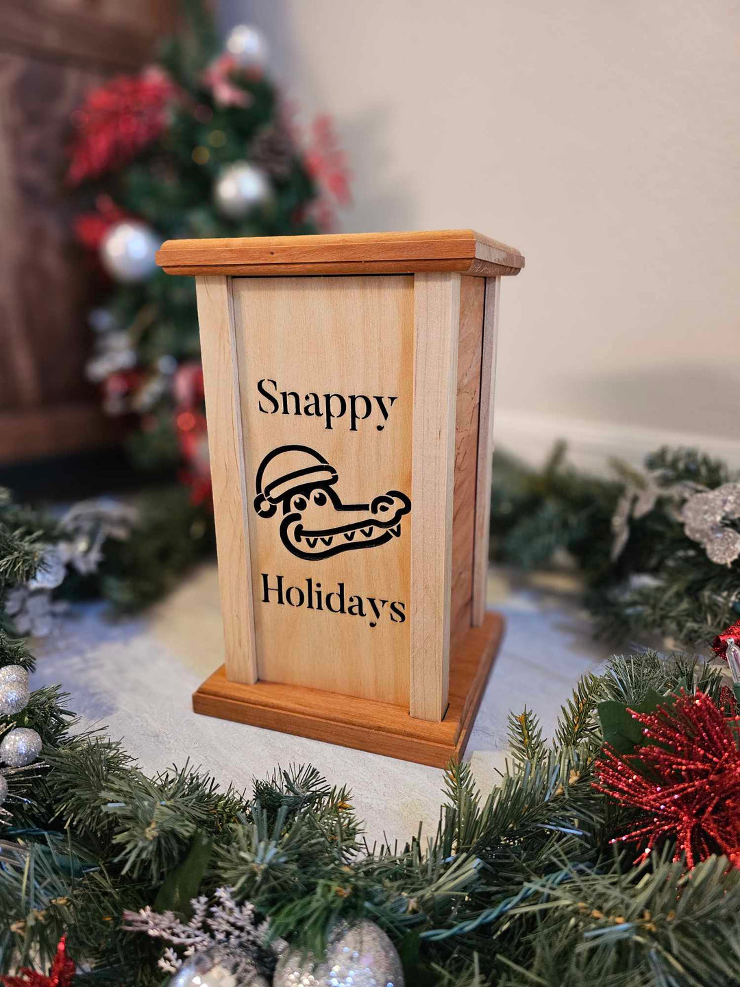 Wooden lantern face showing an alligator in a Santa hat with the words Snappy Holidays.