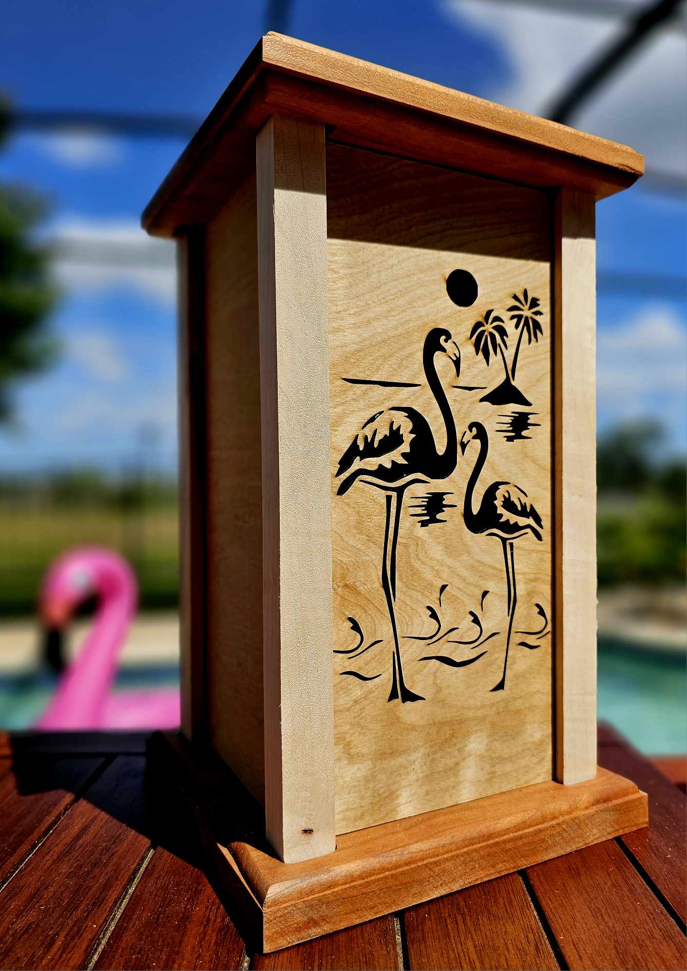 Wooden lantern face showing two flamingos in front of an island and setting sun.